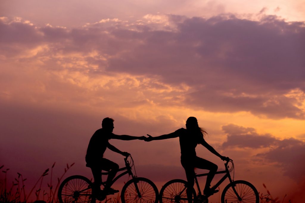 Woman on bike reaching for man's hand behind her also on bike